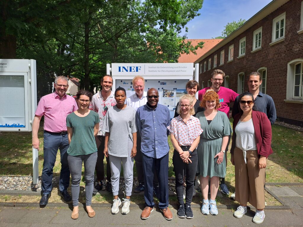 The group of ANCIP researches stand together in front of the INEF institute smiling into the camera on a sunny day.