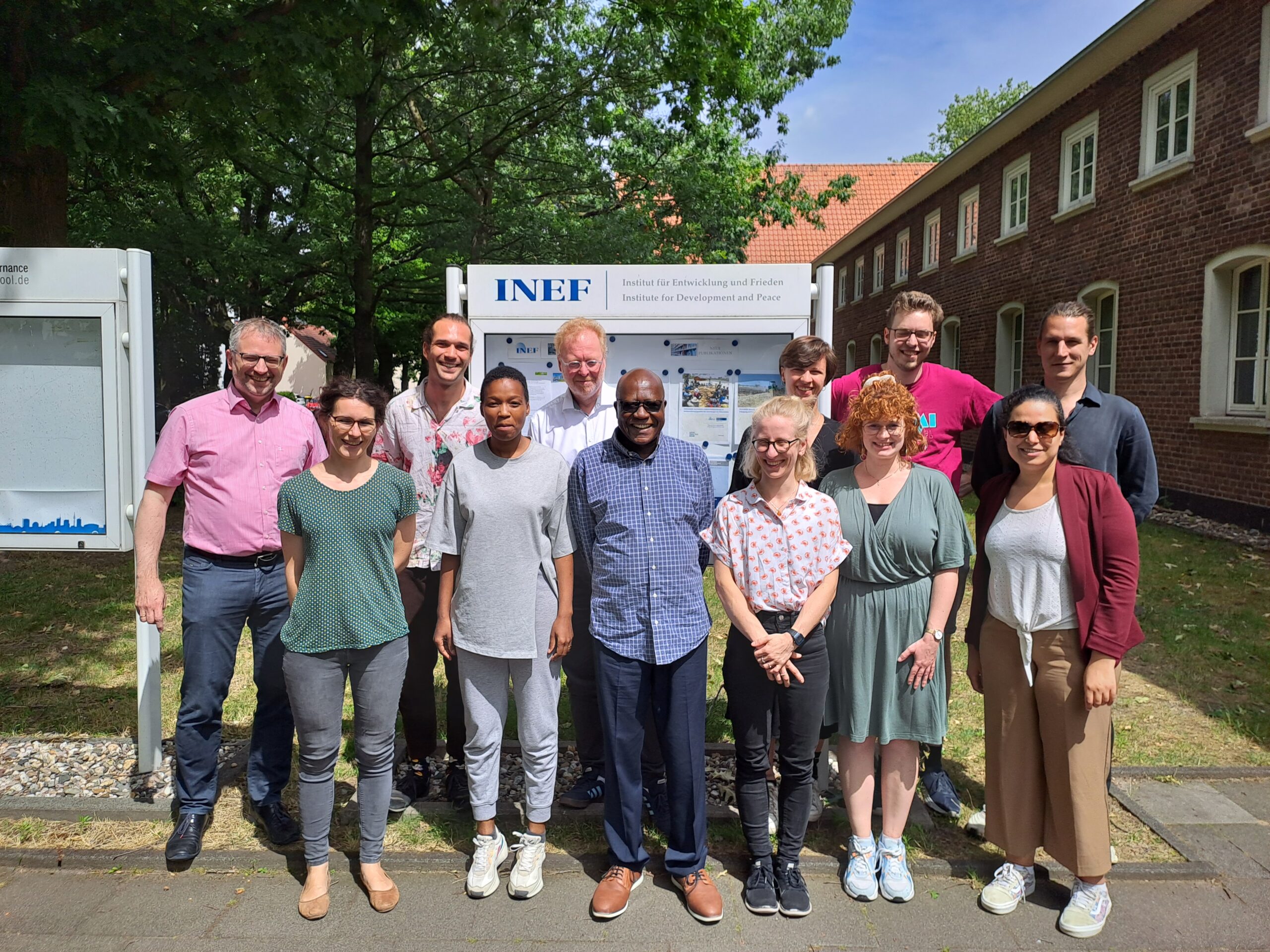 The group of ANCIP researches stand together in front of the INEF institute smiling into the camera on a sunny day.