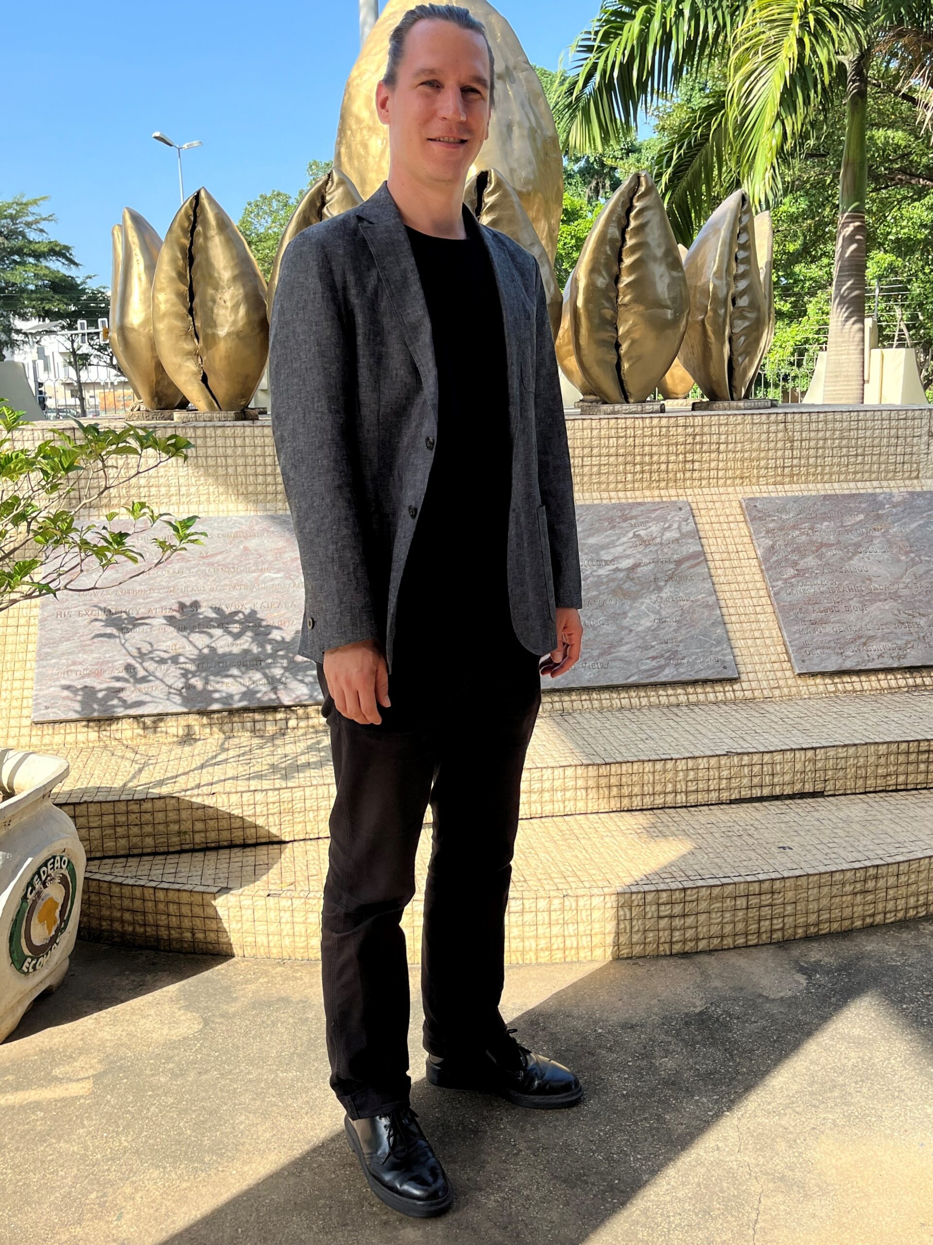 The photo shows Jonas in front of a memorial plaque on the premises of the ECOWAS Commission in Abuja