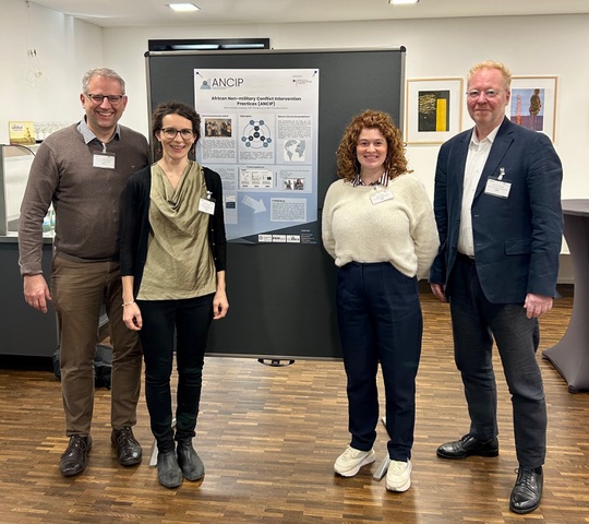 You can see four individuals standing in front of a poster.