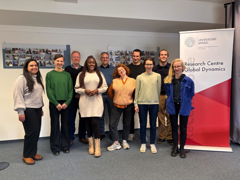 The picture shows the ANCIP Project Members at a venue in the ReCentGlobe Institute, Leipzig University. The members are standing as group, smiling into the camera, with a banner of the ReCentGlobe Institute to the right.