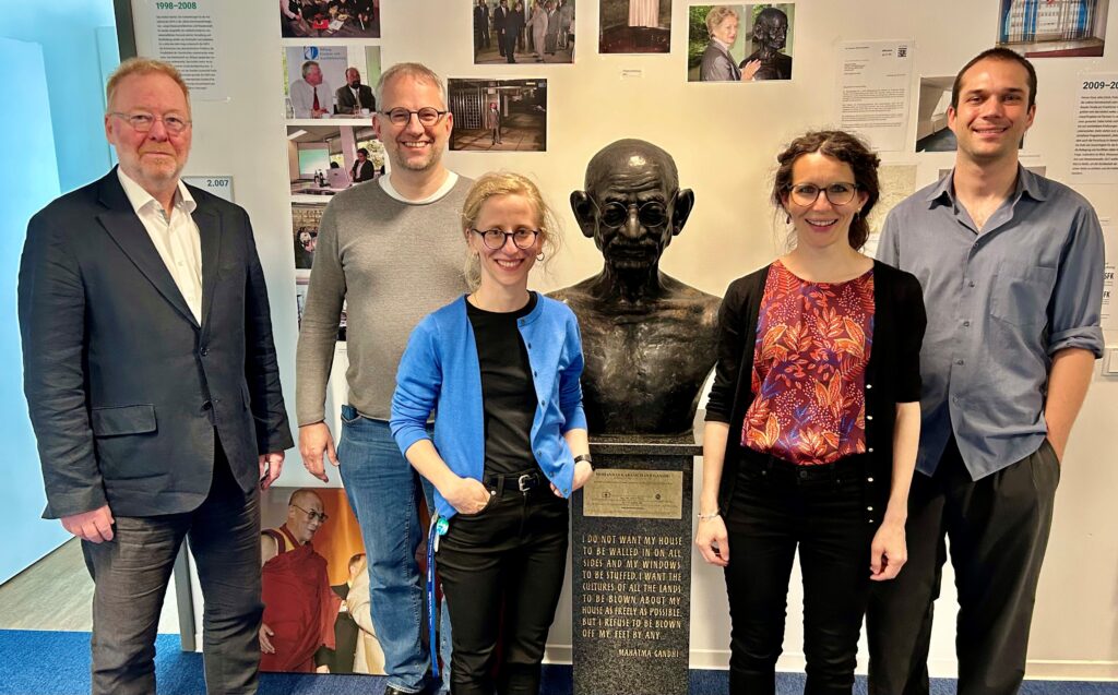 Photo of the ANCIP Team (Ulf Engel, Christof Hartmann, Elisabeth Warnck, Antonia Witt and Vincent Schober) Standing in the PRIF libraries foyier in front of a Mahatma Ghandi bust.
